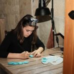 Artist painting small turquoise pieces at a wooden worktable