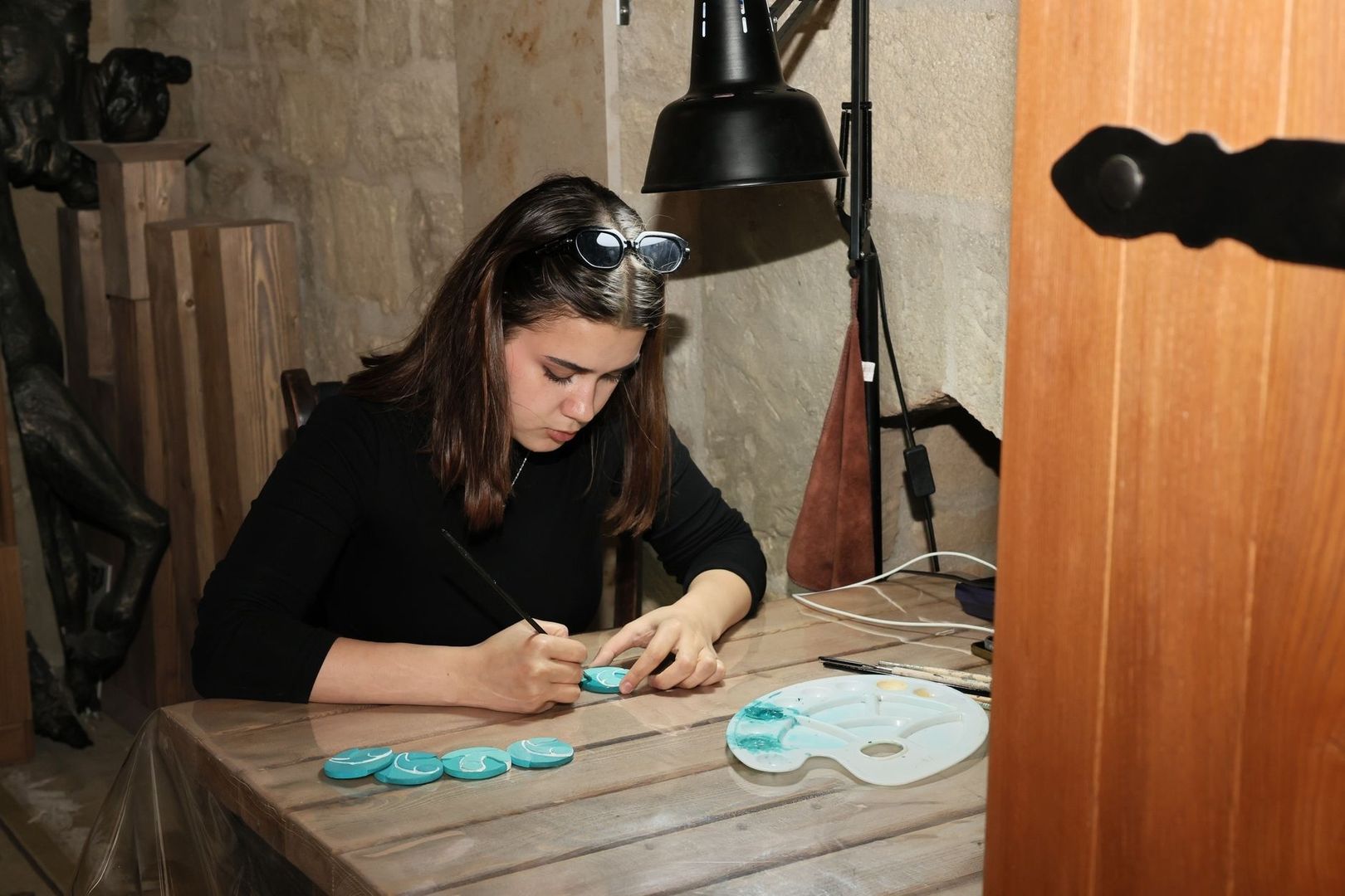Artist painting small turquoise pieces at a wooden worktable