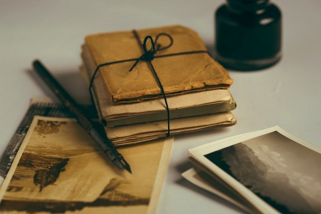 Stack of aged notebooks, photographs, pen, and ink bottle on a desk