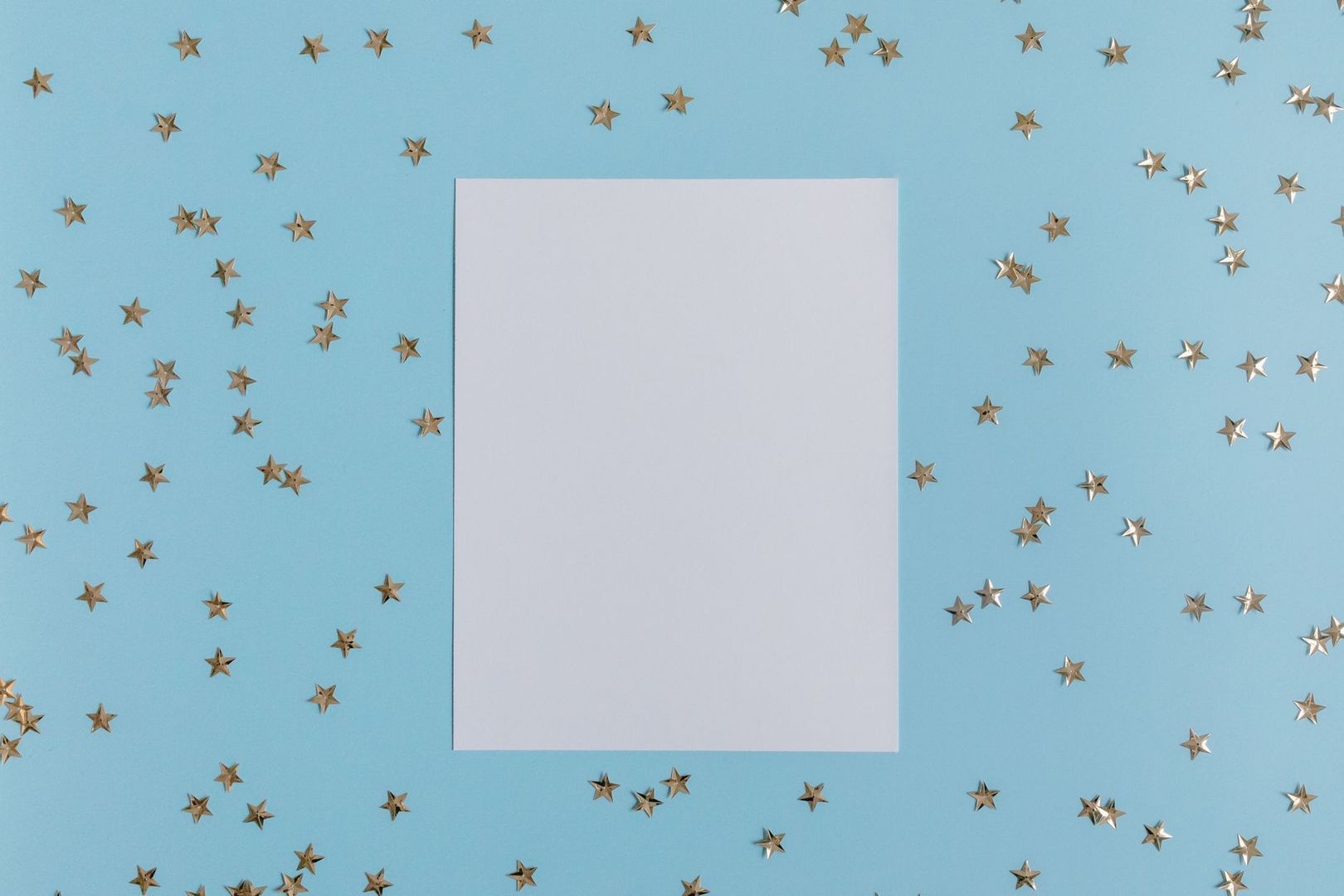 Blank white sheet surrounded by scattered metallic stars on blue